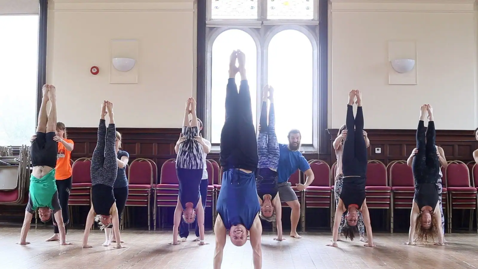 A whole class holding handstands in a line in front of tall arched windows, Ben Lowrey in the middle