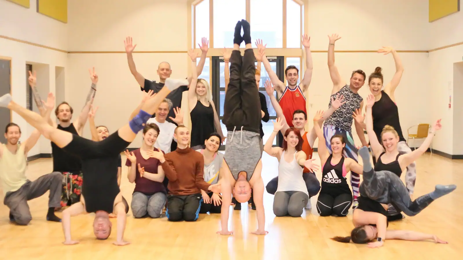 A joyful group waving their arms around Ben Lowrey, who is upside down in a headstand at the front